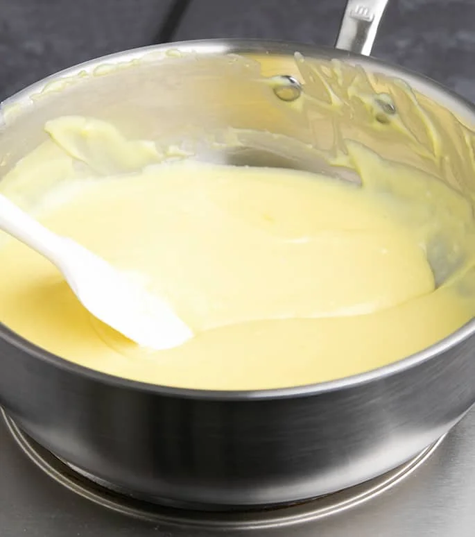 Yellow custard in round pan with white spatula dragging through it