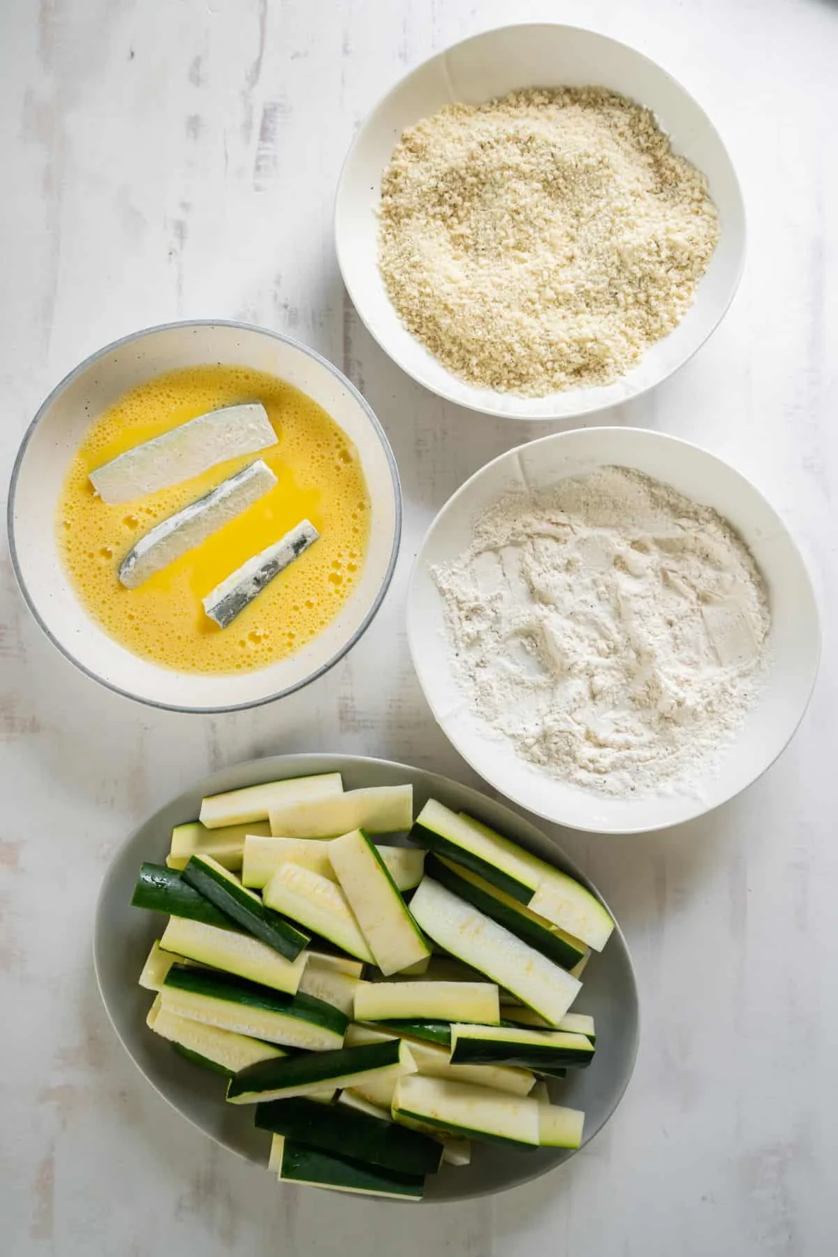 Zucchini fries being dipped into the egg.