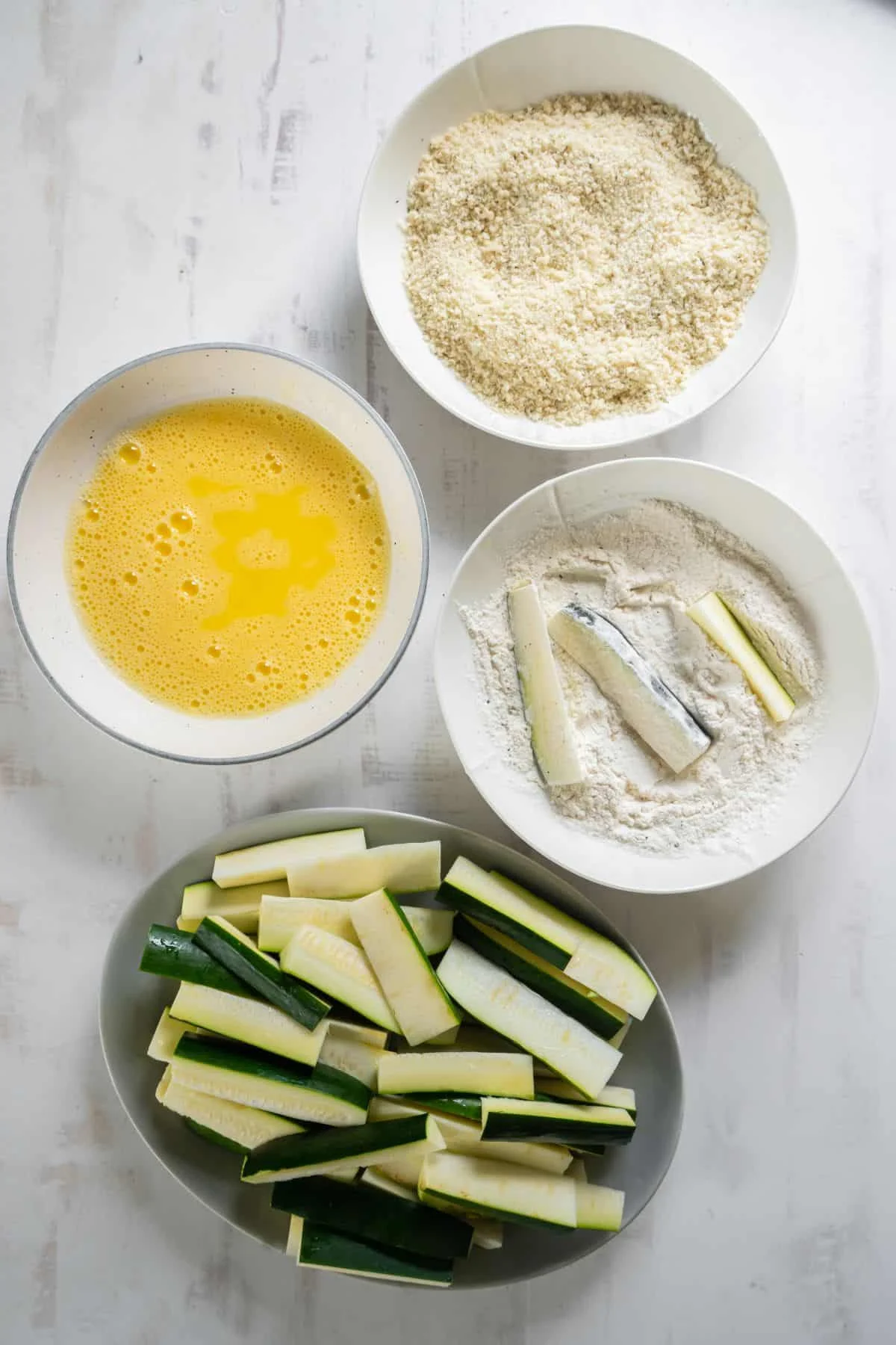 Zucchini sticks being dipped into the flour.