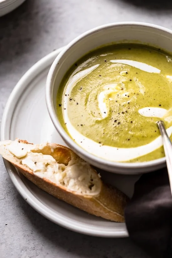 A bowl of cream of broccoli soup drizzled with sour cream next to crusty bread slices.