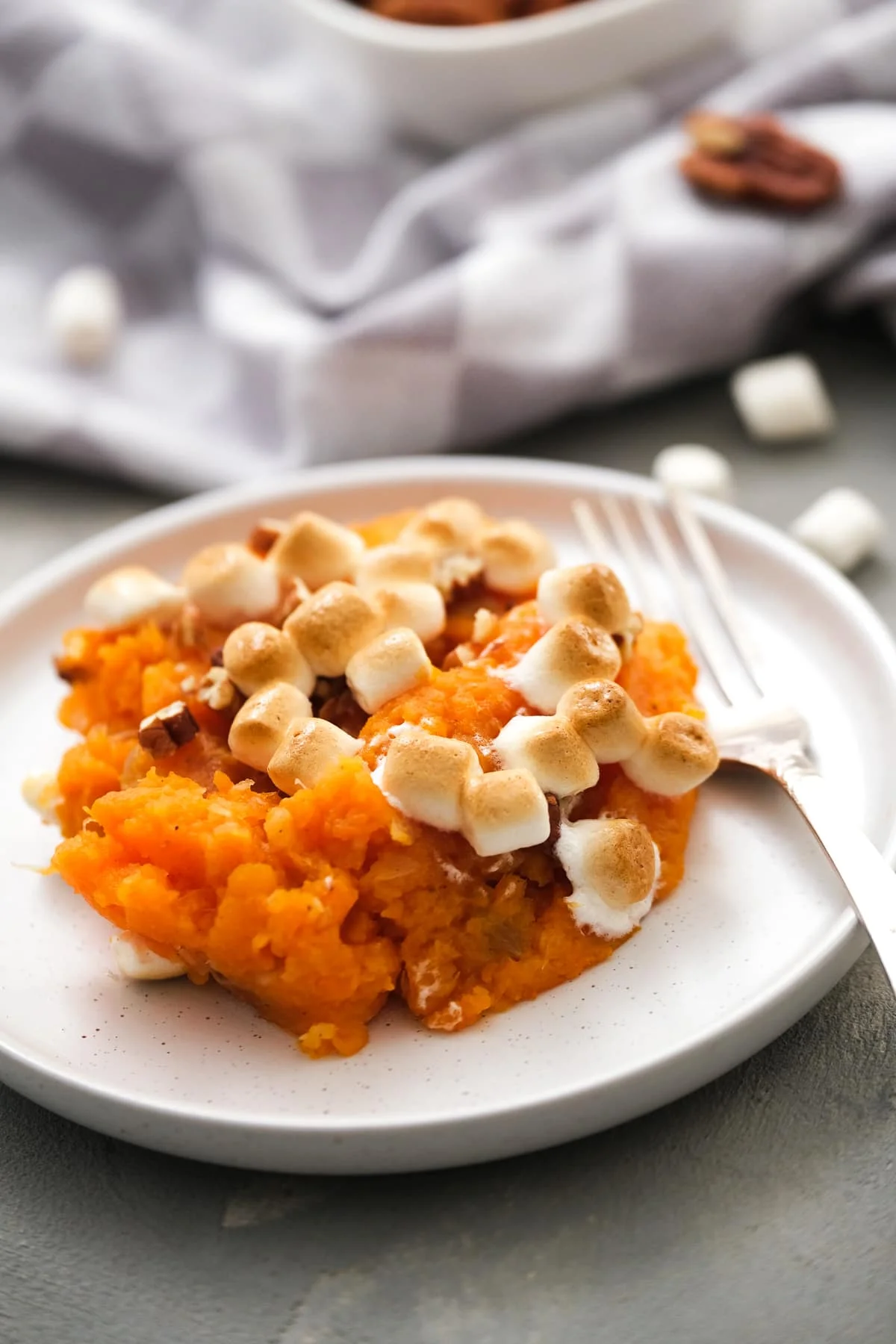 A serving of sweet potato casserole with marshmallows on a plate next to a fork.