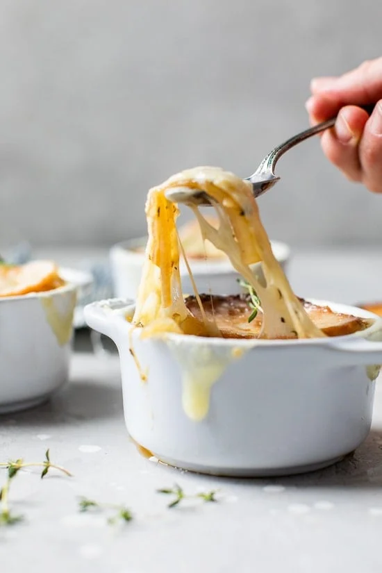 A spoonful of cheesy French onion soup being lifted from a ramekin.
