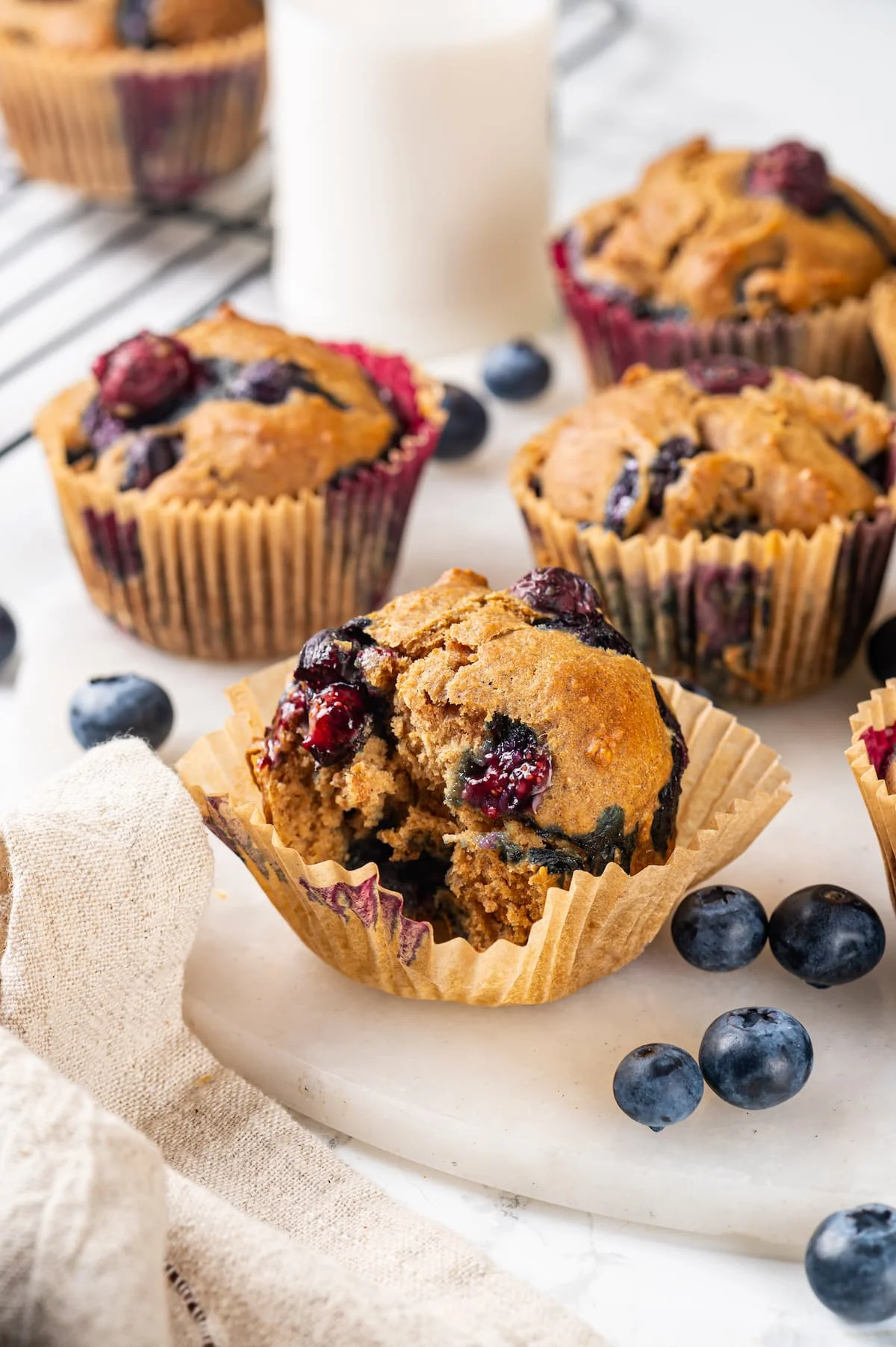 Bitten blueberry muffin in loosened wrapper, with additional muffins in background