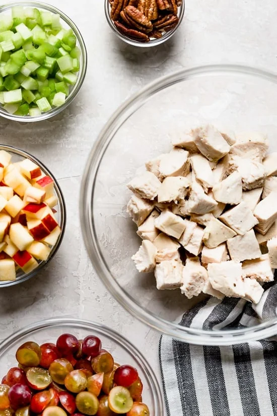 Bowls of chicken, pecans, celery, apples, and grapes.
