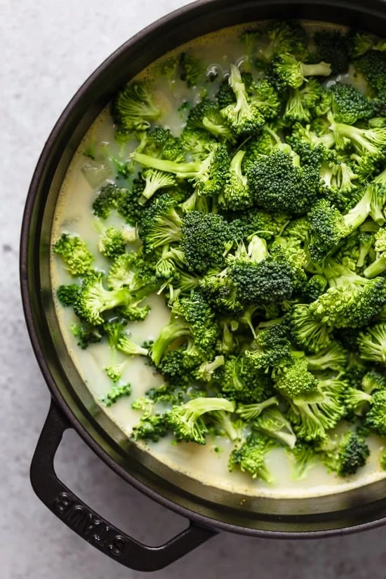 Broccoli florets added to creamy soup in a large pot.