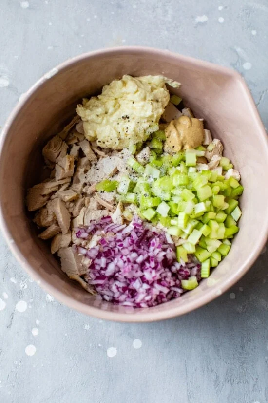 Classic chicken salad ingredients in a bowl include chicken breast, celery, red onion and mayo.