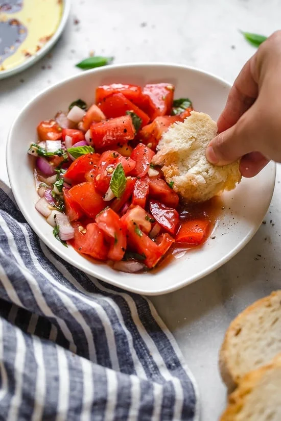 Dipping bread into bowl of summer tomato salad.
