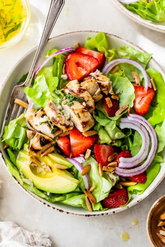 Grilled chicken salad with strawberries, avocado, toasted almonds, and citrus dressing in a bowl.