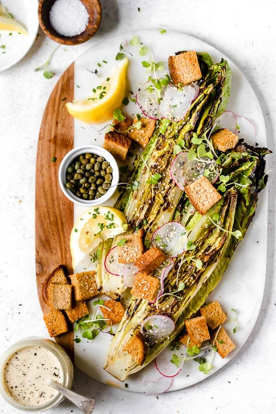 Grilled romaine salad on marble and wood cutting board.