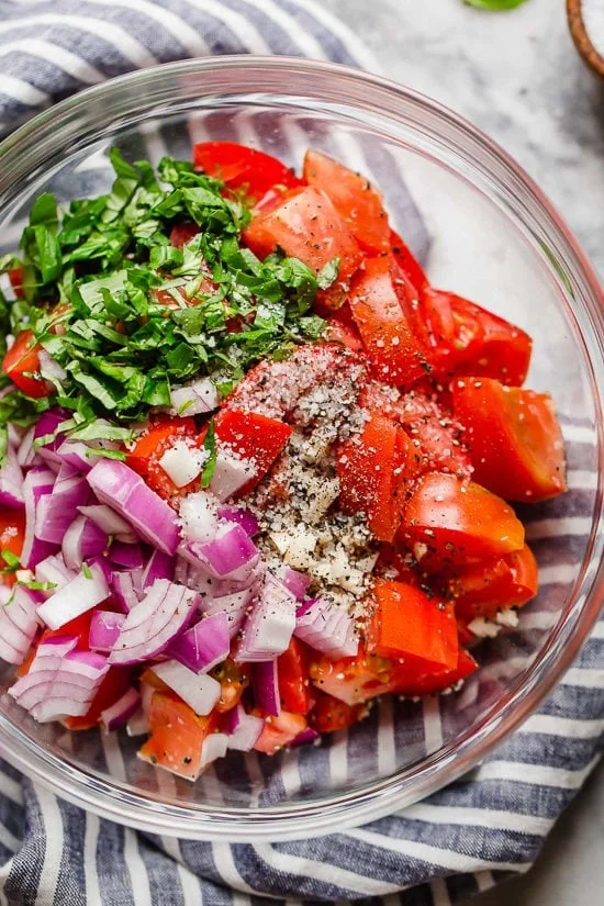 Ingredients for summer tomato salad in glass bowl.