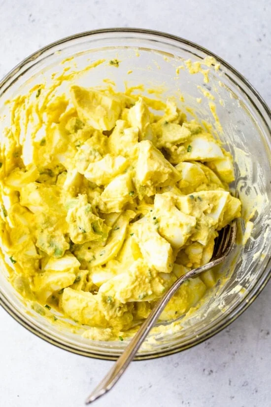 Mixing ingredients for avocado egg salad sandwich in a bowl.