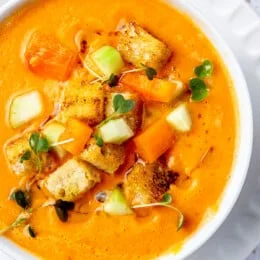 Overhead view of a bowl of gazpacho topped with fresh chopped cucumber, tomato, and crunchy croutons.