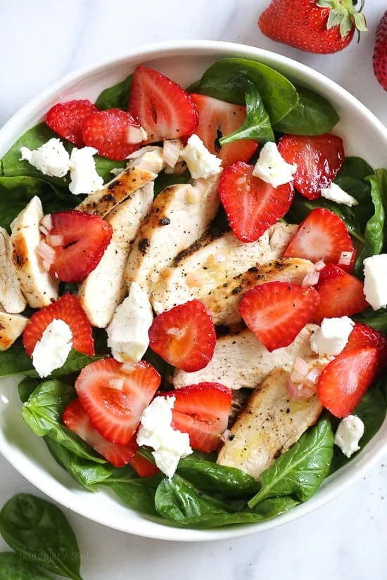 Overhead view of a strawberry chicken salad with spinach and goat cheese in a bowl.