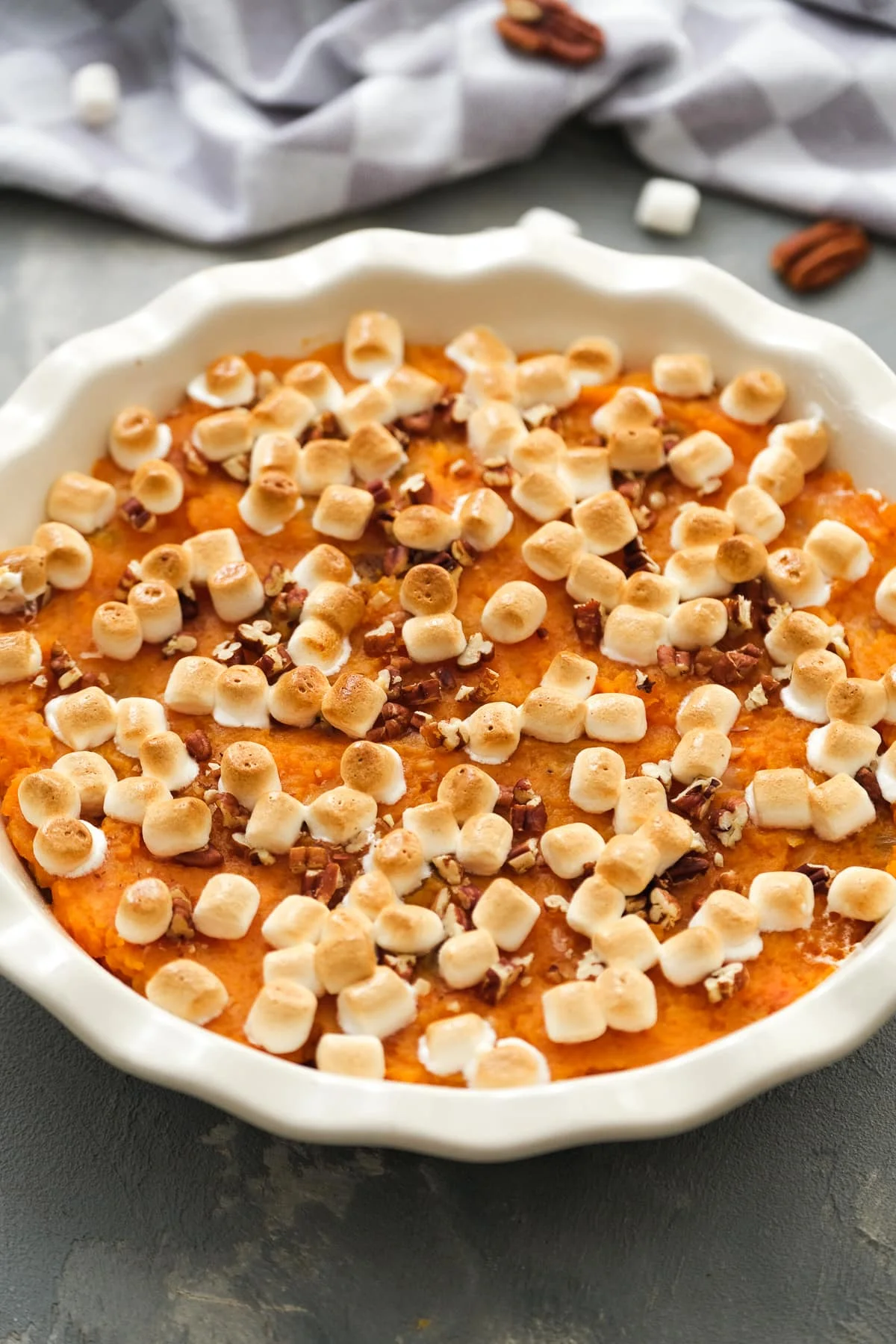 Overhead view of a sweet potato casserole topped with toasted marshmallows and chopped pecans in a round baking dish.