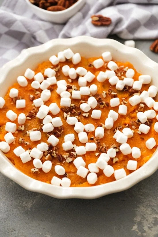 Overhead view of an unbaked sweet potato casserole topped with mini marshmallows and chopped pecans in a round baking dish.