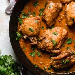Overhead view of boneless chicken thighs in a skillet with shallots in wine sauce with red wine vinegar.