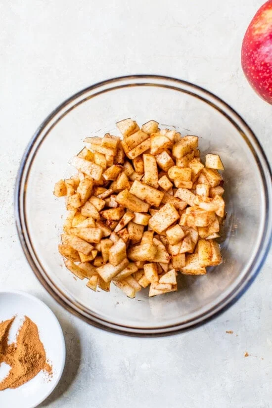 Overhead view of diced apples tossed with lemon juice, cinnamon, and agave in a bowl.