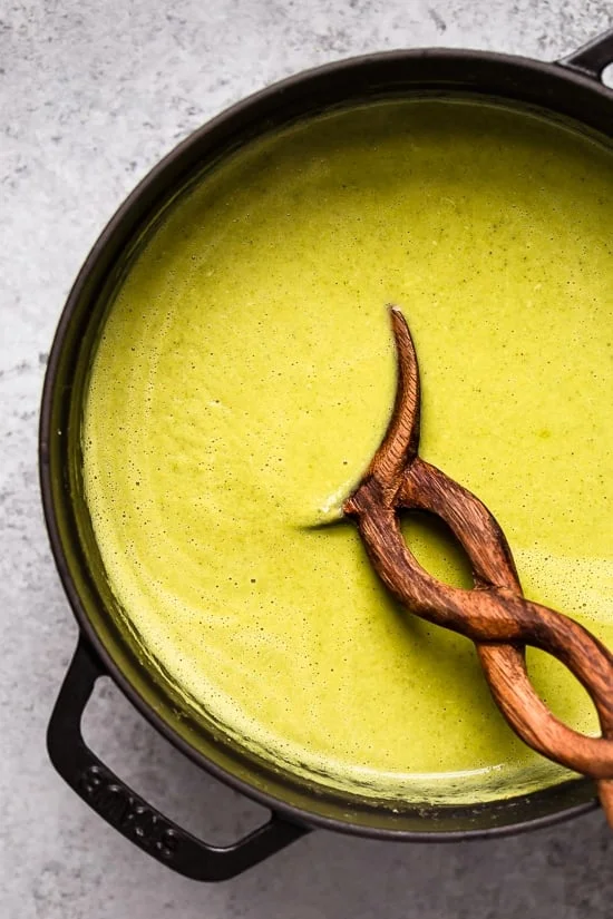 Overhead view of homemade cream of broccoli soup in a pot with a wooden spoon.