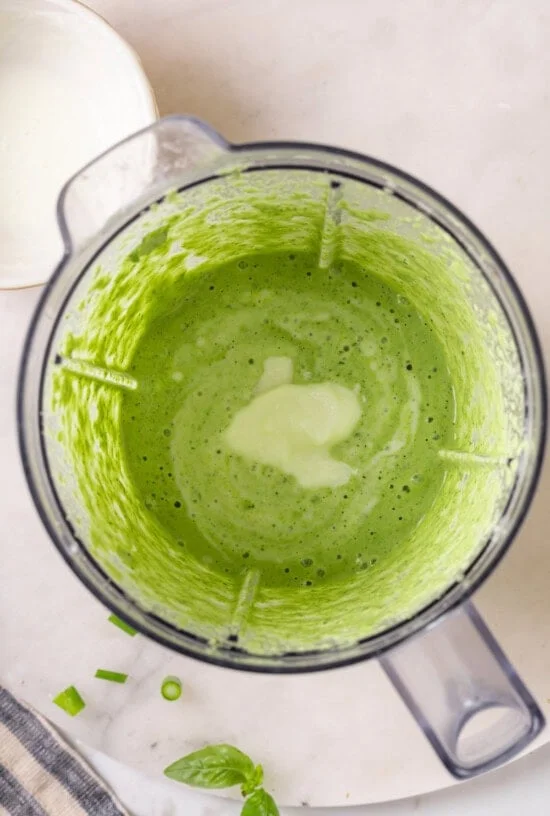Overhead view of sour cream added to blender of basil green goddess dressing