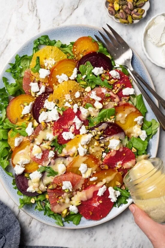 Pouring vinaigrette onto roasted beet and citrus salad.