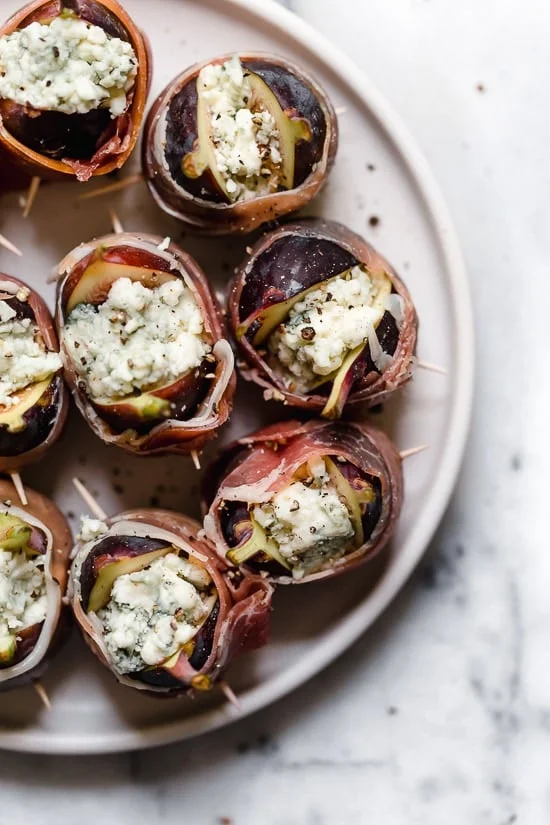 Prosciutto Wrapped Figs with Blue Cheese served on a bed of baby arugula with a light vinaigrette. A delicious combination of salt, acid and sweet.