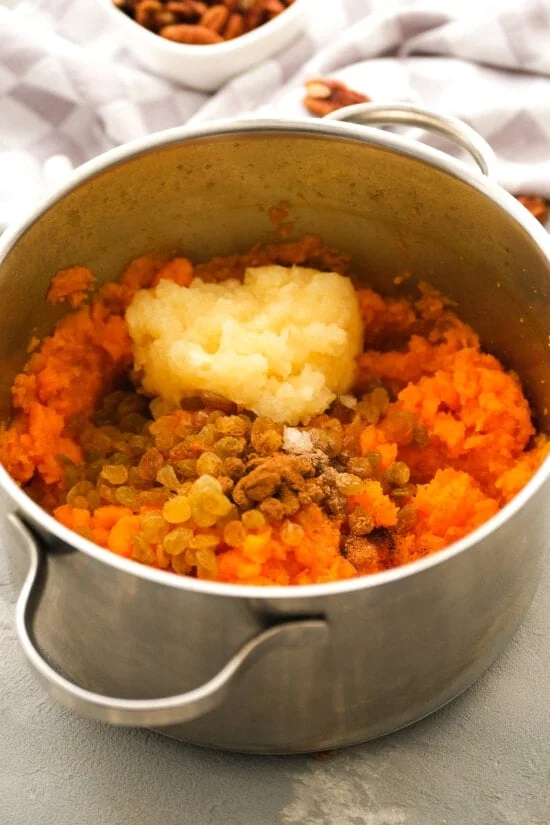 Raisins, spices, and pineapple added to mashed sweet potatoes in a pot.