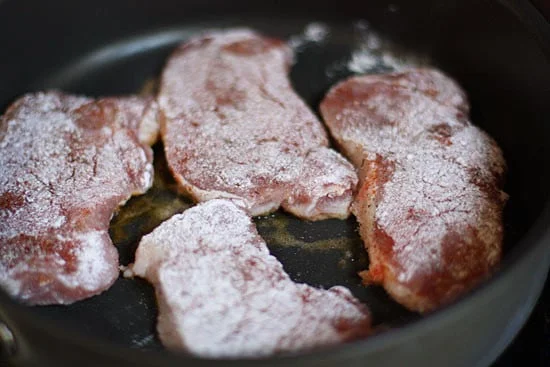 Raw seasoned pork chops placed in pan.