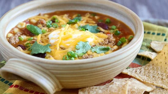 Side view of a bowl of turkey taco soup with sour cream, shredded cheddar cheese, and cilantro.