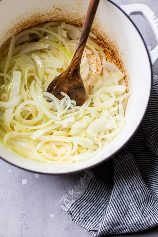Sliced onions being stirred in a pot by a wooden spoon.