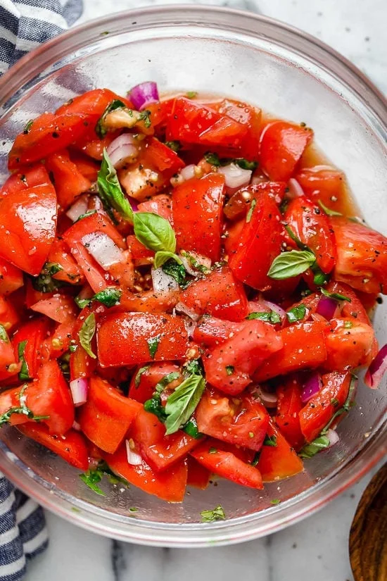 Summer tomato salad in glass bowl with fresh basil and seasonings.