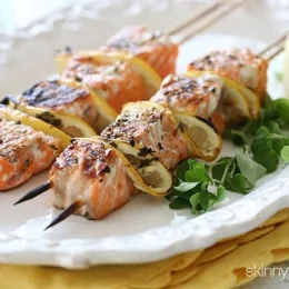 Two grilled salmon kebabs with lemon on a white plate.